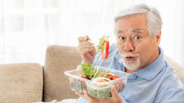 Lifestyle Asian senior man ,old man feel happy enjoy eating diet food fresh salad on sofa