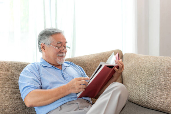 Senior Male reading novel book , smiling feel happy on sofa at home - lifestyle senior elderly people concept