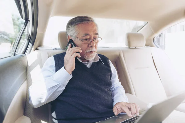 Business senior rich man Stock trader player in suit working with laptop computer and using a smart phone in his car , concept for senior business success