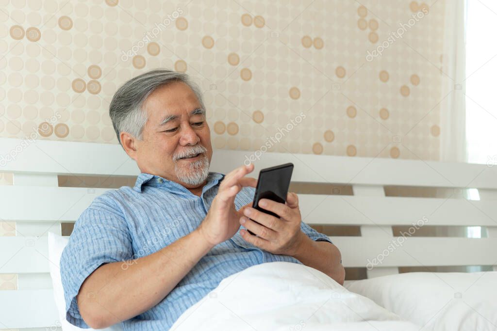 Senior Male using a smartphone , smiling feel happy in bed at home - lifestyle senior concept