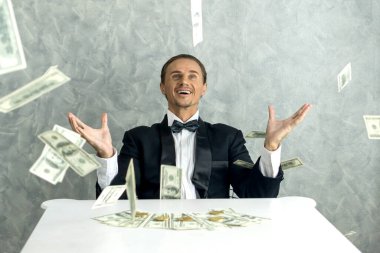 Mutlu iş adamı çok zengin bir adam yağmur parası gibi dolarları havaya fırlatır ve Amerikan dolarını masaya yatırır - iş başarısı konsepti