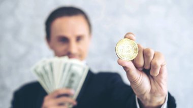 İş adamı zengini tüccar Bitcoin altın sikkesi tutuyor Bitcoin tüccarı için yeni para değişimi ve masa başı iş konsepti üzerine Amerikan doları banknotları