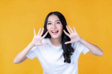 Güzel Asyalı genç kadın çığlıkları iyi haberi ya da terfiyi duyurur. Ağzı açık bir şekilde yüzüne yakın el ele tutuşur. Sarı arka planda izole edilmiş Herald haber terfisi.