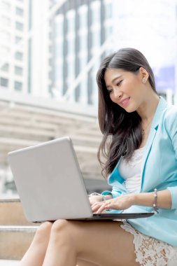 İş kadını kıyafetleriyle gülümseyen güzel kız dizüstü bilgisayar kullanıyor, şehir geçmişi var.