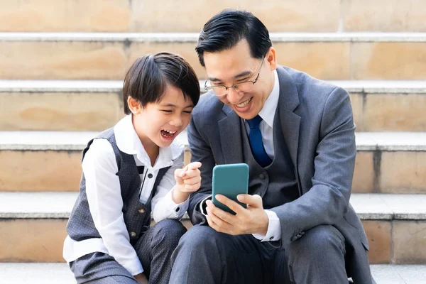 Father and son playing  smart phone together on business district urban, Dad and Son happy Asian family concept