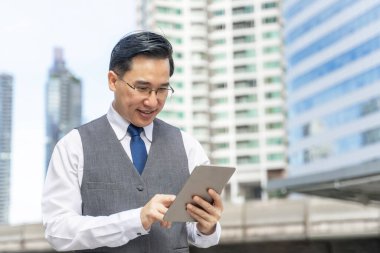 İş dünyasından Asyalı bir adam iş bölgesi kentlerinde tablet bilgisayar kullanıyor - yaşam tarzı iş insanları kavramı