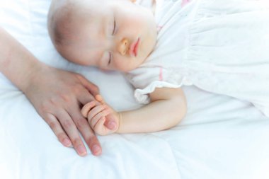 Seçici odak noktası, yeni doğmuş küçük bebek beyaz bir yatakta uyuyordu ve annesinin parmağını tutarak kendini güvende ve mutlu hissediyordu.