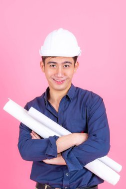 Beyaz miğfer takan ve elinde eskizler tutan genç mimar, pembe arka planda gülümseyerek ayakta duruyor.