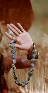 Geleneksel bir kolye tutan Afrikalı bir elin fotoğrafı.