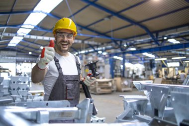 Fabrika işçisinin portresi. Koruyucu ekipman. Prodüksiyon salonunda baş parmak tutuyor..