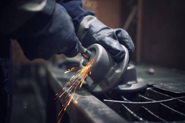Öğütücü ile metal parçaları şekillendiren fabrika işçisi. Kıvılcımlar uçuşuyor.