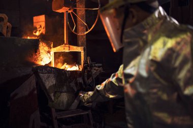 Koruyucu giysiler içindeki işçi dökümhanede erimiş demiri kontrol ediyor..