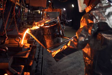 Oyuncu seçimi ve dökümhane. Koruyucu kıyafetli işçiler kalıplara sıvı çelik döküyorlar. Metalurji ve çelik üretimi.