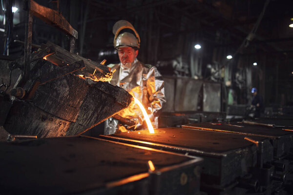 Foundry workman pouring molten iron into molds for steel production. Heavy industry and metallurgy process.