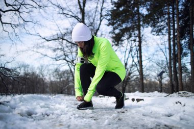 Spor elbiseli bir kadın kışın parkta ayakkabı bağı bağlıyor. Fitness ve eğlence.