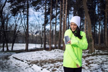 Kışın giyinen sporcu kadın, kar yağarken parkta antrenman yapmadan önce şarkı seçiyor..