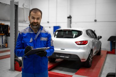 Hizmet ve bakım için araç atölyesinde duran orta yaşlı bir araba tamircisinin portresi.