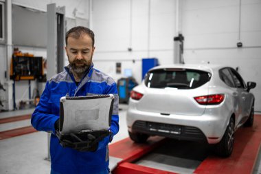 Hizmet ve bakım için araç atölyesinde dizüstü bilgisayarı olan orta yaşlı bir araba tamircisinin portresi.