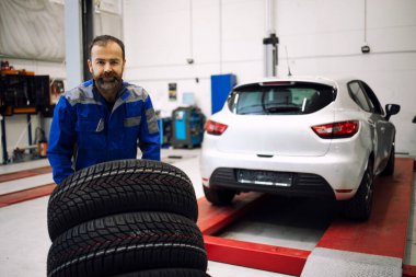 Yeni lastikleri olan profesyonel araba tamircisi atölyede duruyor. Kış ya da yaz mevsimi için lastik değiştirmek.