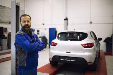 Araç atölyesinde kollarını kavuşturmuş duran profesyonel araba tamircisinin portresi..