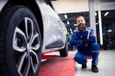 Profesyonel araba tamircisinin portresi bir otomobilin yanında duruyor ve ingiliz anahtarı araçları tutuyor..