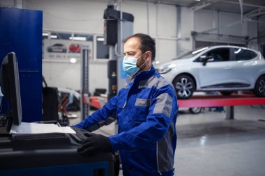 Corona virüsü salgını sırasında araç atölyesinde çalışan yüz koruma maskeli profesyonel araba tamircisi. Otomobil servisi ve bakımı.