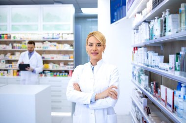 Eczanede ya da eczanede kolları kavuşturulmuş duran güzel sarışın eczacının portresi. Arka plandaki raflarda ilaçlarla.