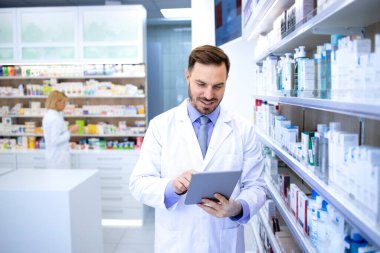 Eczanede ya da eczanede çalışan profesyonel yakışıklı bir eczacı. Tablet bilgisayarındaki ilaçları kontrol ediyor. Sağlık ve eczacı.