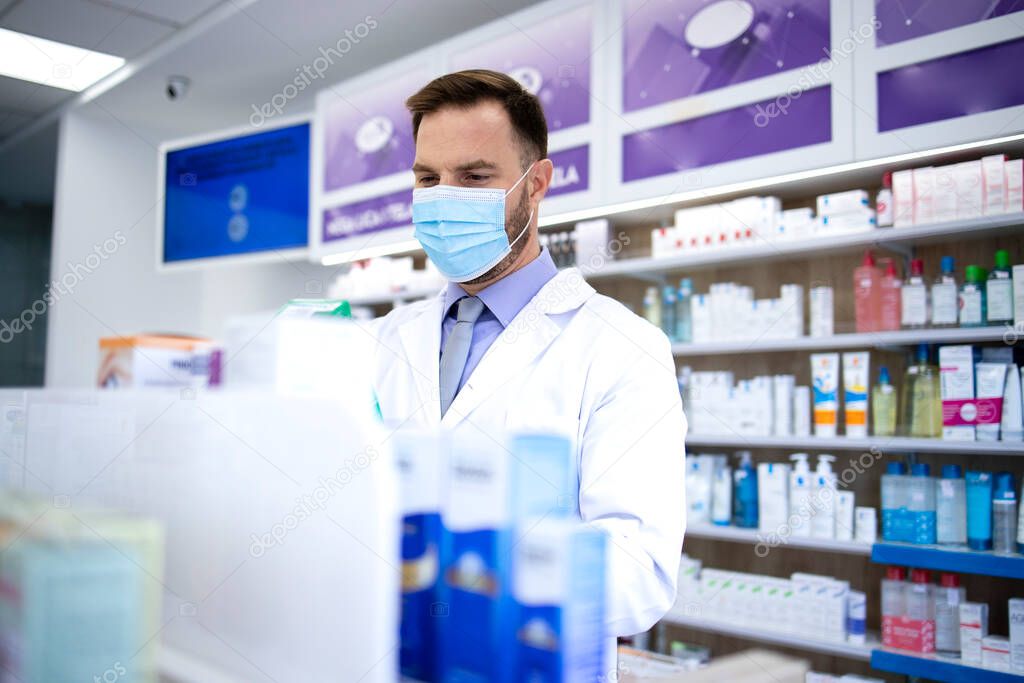 Pharmacist wearing face mask and white coat working in drug store during corona virus pandemic. Healthcare and medicine.