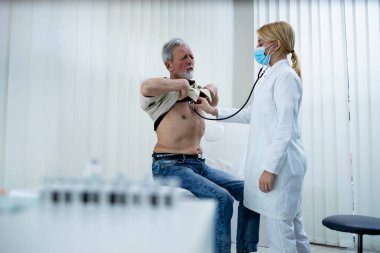 Doktor yaşlı adamın solunum sistemini ve ciğerlerini stetoskopla kontrol ediyor..