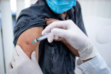 Corona virüsü salgını sırasında yaşlı bir adamın koluna aşı vurulmasını yakından izleyin..