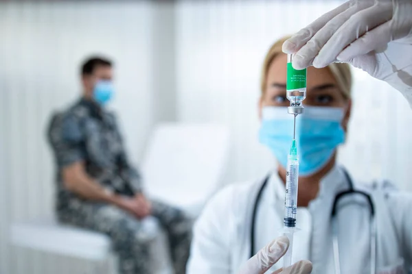 Vaccination of the military against corona virus. Doctor holding bottle and syringe and preparing vaccine shot for the soldier in uniform during corona virus epidemic.