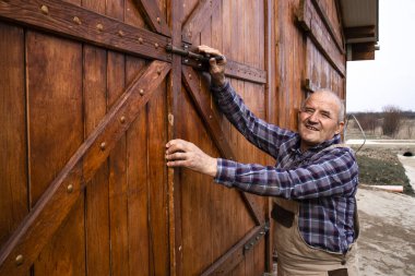 Çiftçi portresi, evcil hayvan çiftliğinin ahşap çiftlik kapılarını kapatıyor..