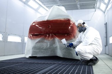 Koruyucu giysileri ve maskeli profesyonel araba ressamı portresi boyalı tabanca tutuyor ve arabada bekliyor..