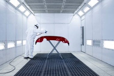 Koruyucu giysiler içinde profesyonel bir araç ressamı. Otomobil tamponunu basınçlı silahla boyuyor..