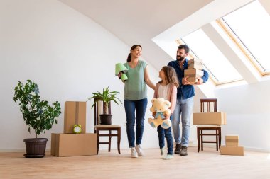 Happy caucasian family moving in new apartment with cute little girl carrying boxes and belongings.