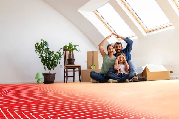 Home, people, moving and floor heating concept - portrait of happy family sitting on warm parquet with floor heating and pipes.