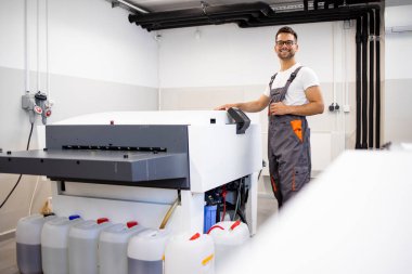 Gülümseyen işçi matbaada bilgisayardan tabak makinesine çalışıyor..