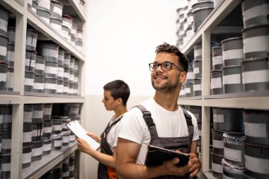 Rafları olan bir depo. Boya kutuları ve boyacılar envanter çıkarıyor..