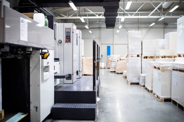 Matbaa veya fabrika içi modern ofset kağıt makinesi ve arka planda çarşaf yığınları.