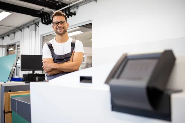 印刷厂里站在计算机与印表机旁边微笑的印刷工人的画像 — 图库照片