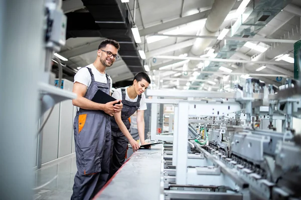Baskı fabrikasındaki modern ambalaj makinesinin üretim sürecini kontrol eden üretim hattı işçileri.