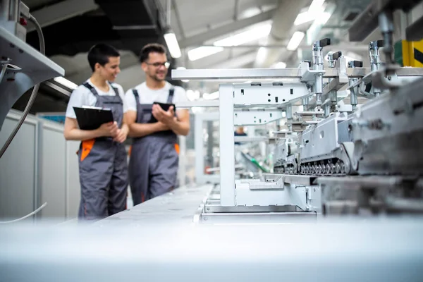 Üretim hattı işçileri fabrikadaki modern ambalaj makinesinin üretim sürecini kontrol ediyorlar.