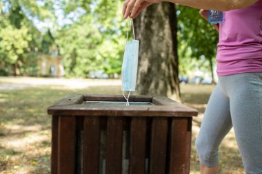 Tanınmayan kişi kullanılmış yüz koruma maskesini çöp kutusuna atıyor..
