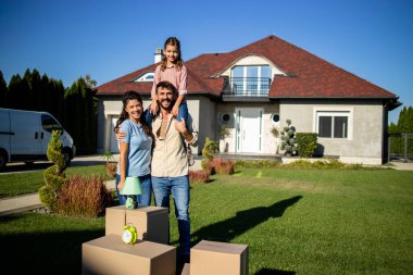 Karton kutuların ve yeni evin yanında taşınmaya hazır bir ailenin fotoğrafı..