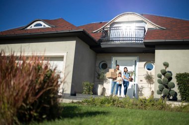 Yeni evlerinin verandasında taşınmaya hazır mutlu beyaz bir ailenin portresi..