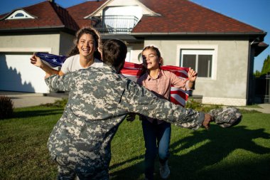 Üniformalı asker eve geliyor ve Amerikan bayrağıyla sevgili ailesi kollarına koşuyor..