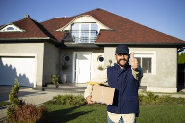 Üniformalı bir teslimatçının portresi. Elinde başparmaklar var ve paketleri adrese teslim ediyor..