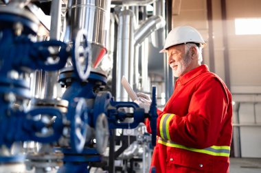 Kıdemli bakım işçisi endüstriyel ekipmanları ve kontrol sistemini tabletle kontrol ediyor..