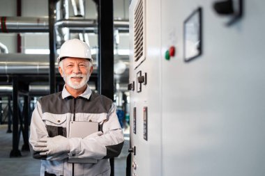Endüstriyel fabrikada çalışan kıdemli erkek mühendis, elinde dijital tablet tutuyor.